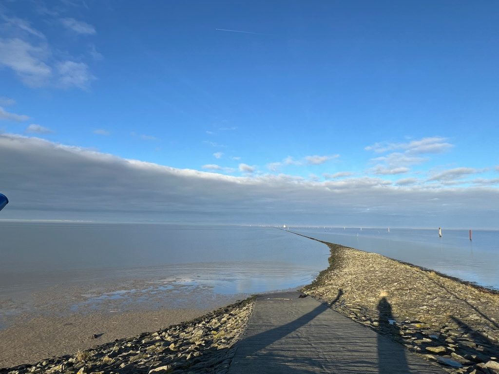 Scenic view of the North Sea coastline in Esens, Germany, with a narrow stone path leading into the water under a blue sky.