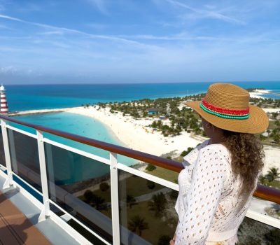 Image for Woman in sun hat admiring tropical island view from cruise ship balcony near beach and lighthouse