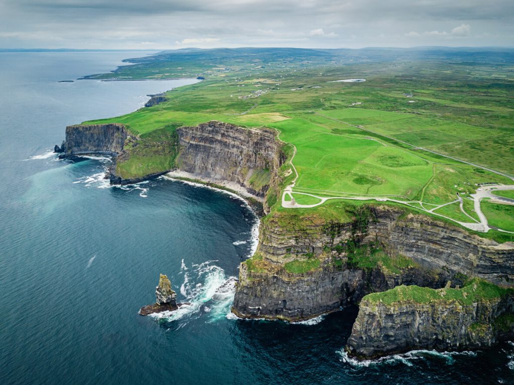 Aerial view of the Cliffs of Moher in Ireland with dramatic limestone cliffs, lush green fields, and the Atlantic Ocean below.